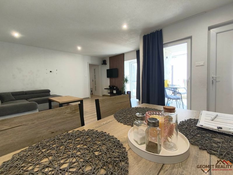 Dining table with decorations, sofa, television, and wooden decor flooring in a family house.