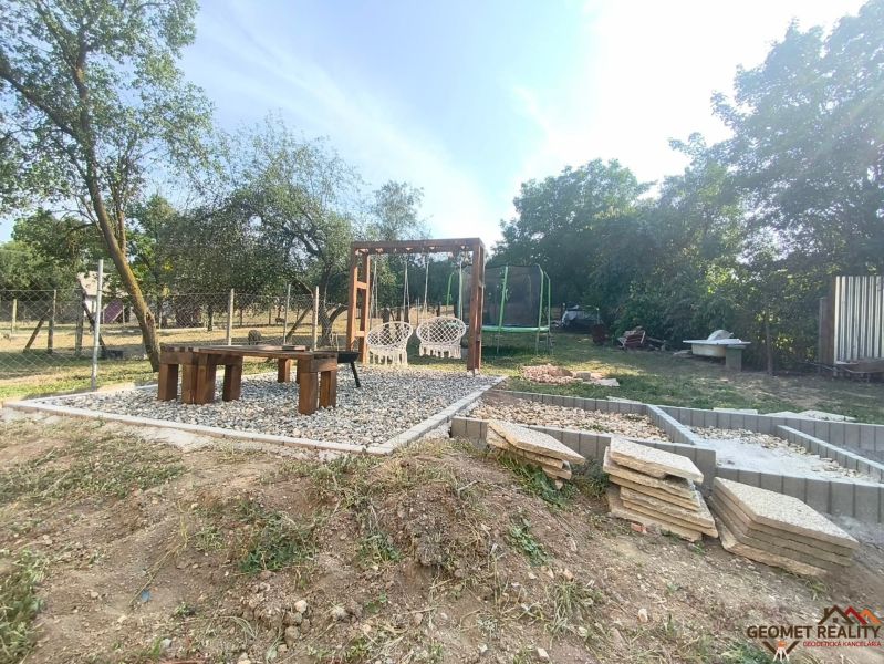 The courtyard of a family house in Dobroč with swings, seating, and a trampoline surrounded by greenery.