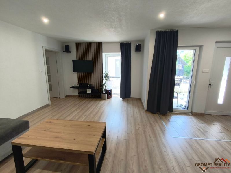Living room in a family house with wood-patterned flooring, a television, and dark curtains.