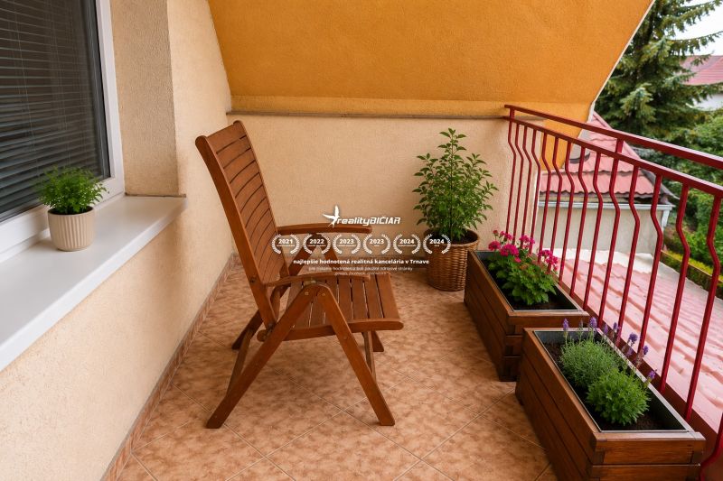 A balcony of a family house with a wooden chair, flowers, and a view of the rooftops in Sereď on Hrnčiarska Street.