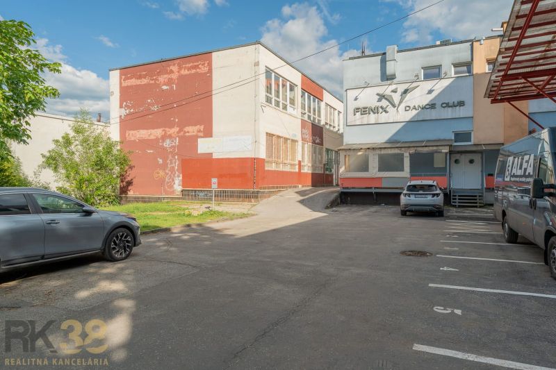A building in Banská Bystrica with parked cars in front of the dance club in the parking lot.