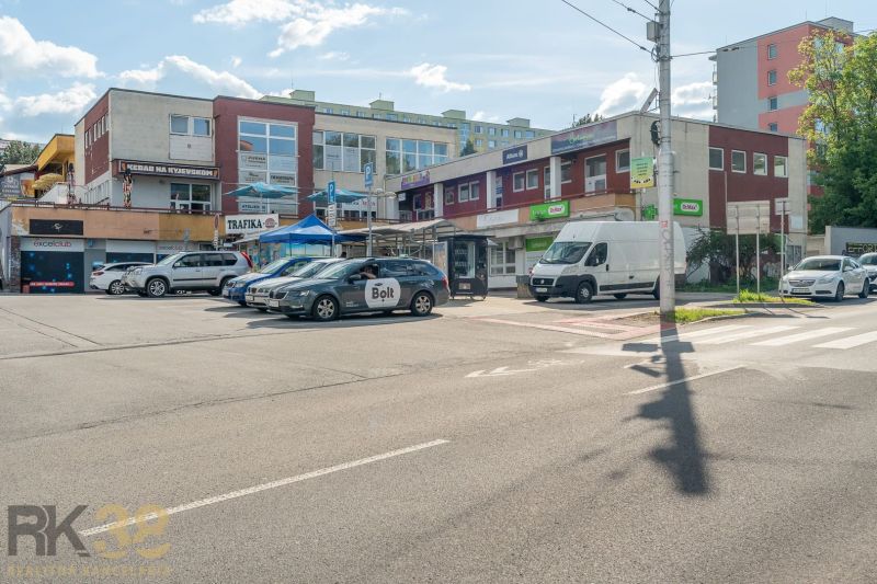 A street with a building in Banská Bystrica, cars, and advertising signs on businesses.