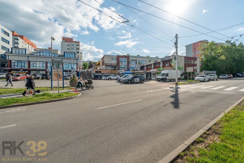 A street in Banská Bystrica with buildings, cars, and passing people.