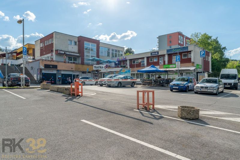 A parking lot with shops and a restaurant in Banská Bystrica, with cars parked around.