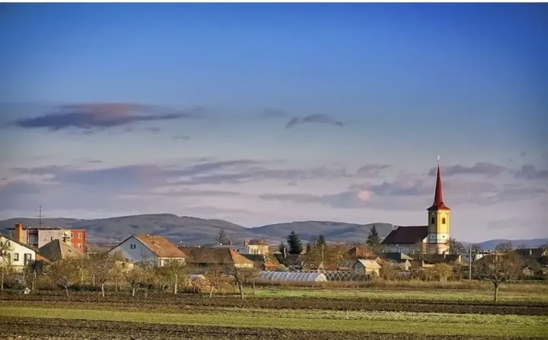 A village with a church in Kamenný Most surrounded by agricultural and forest lands.