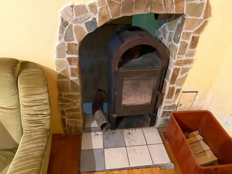 A wood-burning stove in a family house with a wooden decor floor next to a comfortable armchair.