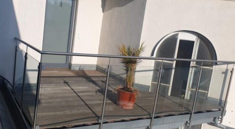 A balcony with glass railing and a potted plant in a 2-room apartment.