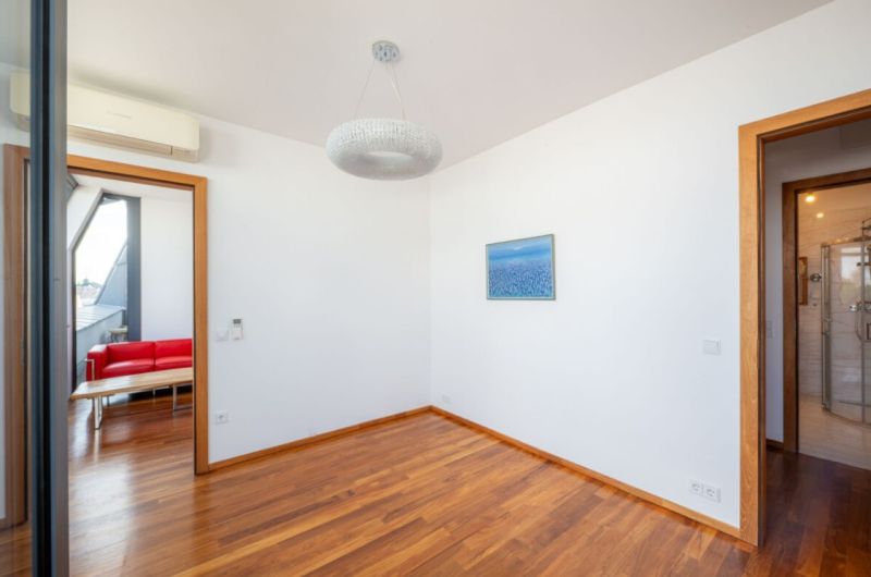 A room with a wooden floor, a chandelier, and a painting in a two-room apartment.