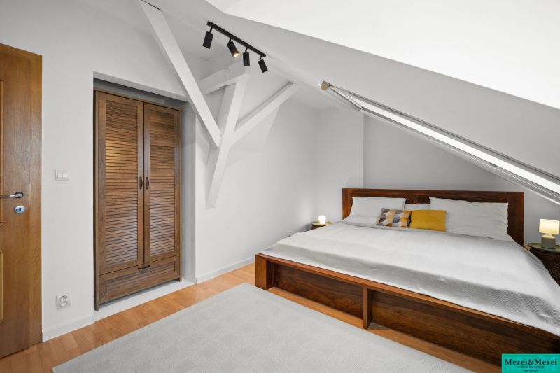 Bedroom with a double bed, sloped ceiling, wood-patterned floor, built-in wardrobe.