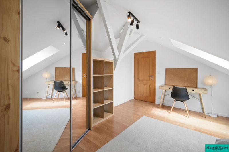 Attic room with a table, black chair, mirrored wardrobe, and wooden decor flooring.