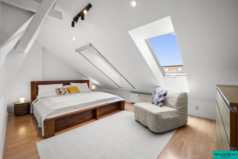 Attic bedroom with a large bed, armchair, and floor with wooden decor.