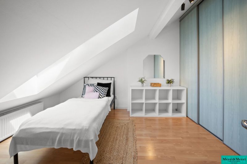 Attic bedroom with a single bed, wooden decor flooring, and storage spaces.