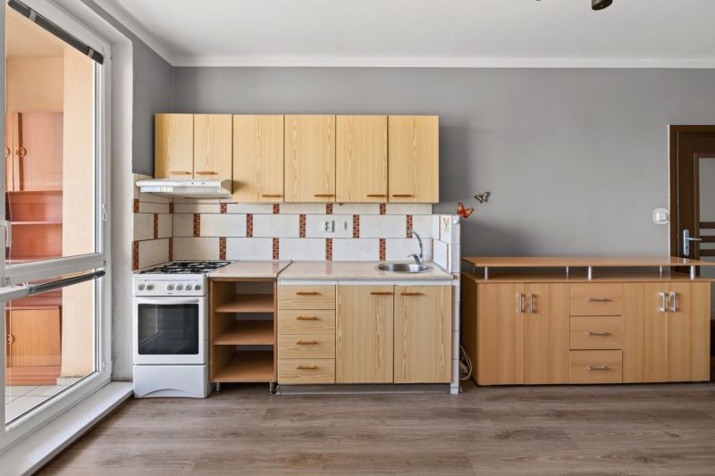 A kitchen in a studio apartment with a wood-patterned floor and wooden cabinets.