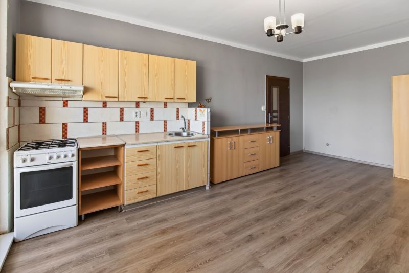 A kitchen in a studio apartment with a wood-patterned floor and light-colored furniture.