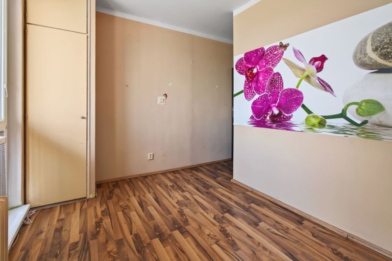 A room in a one-room apartment with a wooden decor floor and floral wall decoration.