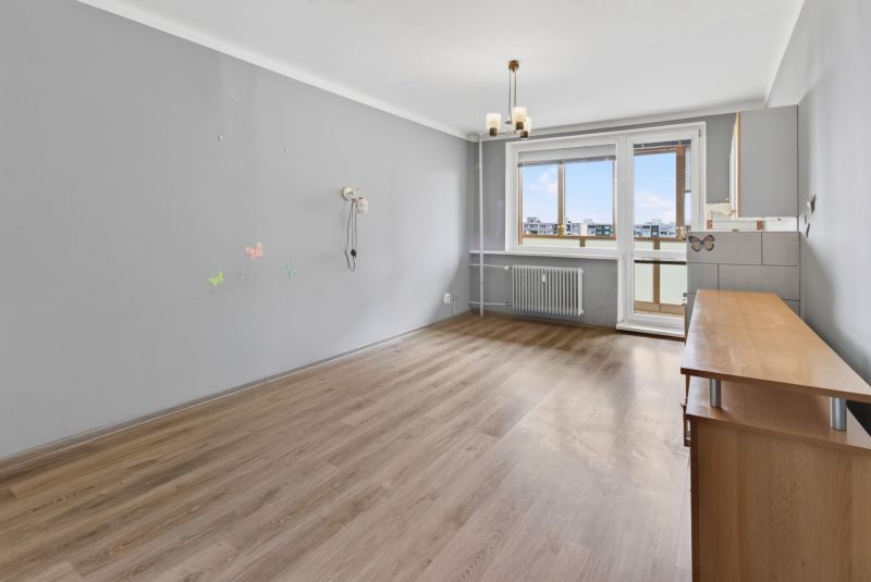 Living room with wood-patterned flooring in a studio apartment, gray walls, window with radiator.
