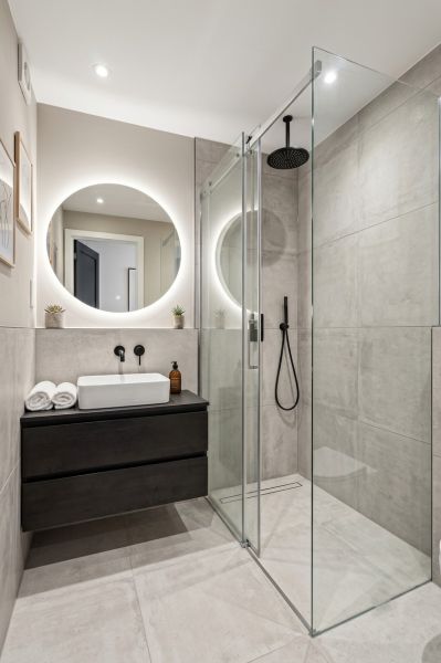 A bathroom in a studio apartment with a modern shower and a round mirror.