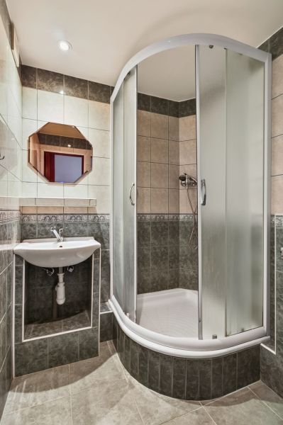 A bathroom with tiles, a shower corner, and a sink in a studio apartment.
