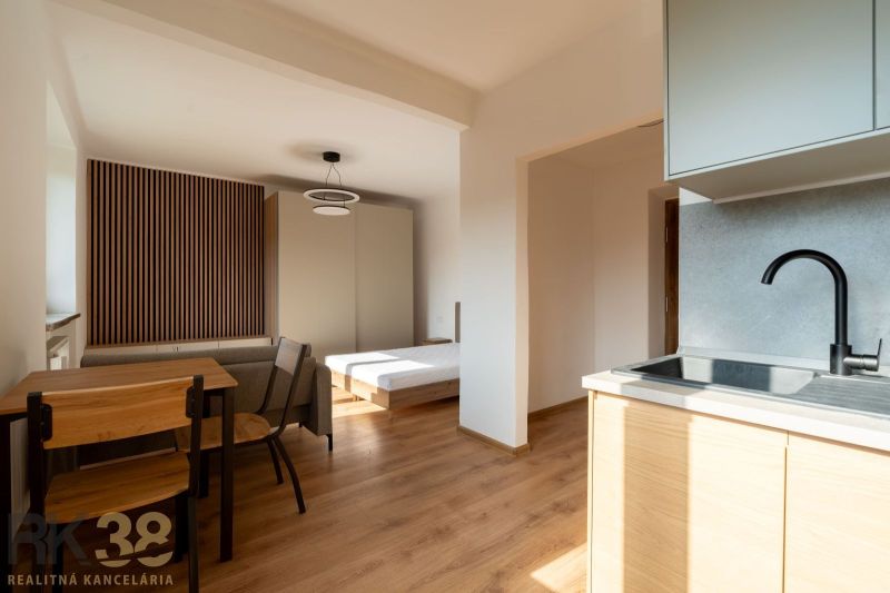 A kitchen with a kitchen unit, a dining table, and a bed, with a wooden decor floor.