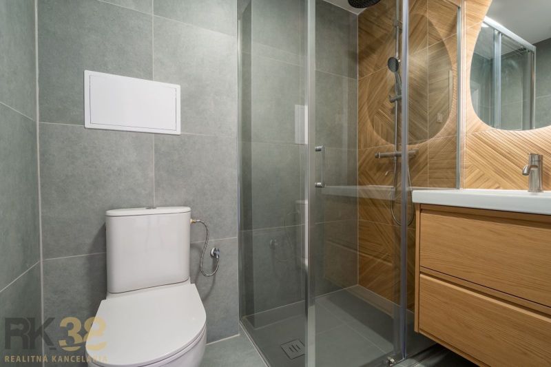 A bathroom in a studio apartment with a shower and a toilet, tiled with large tiles.