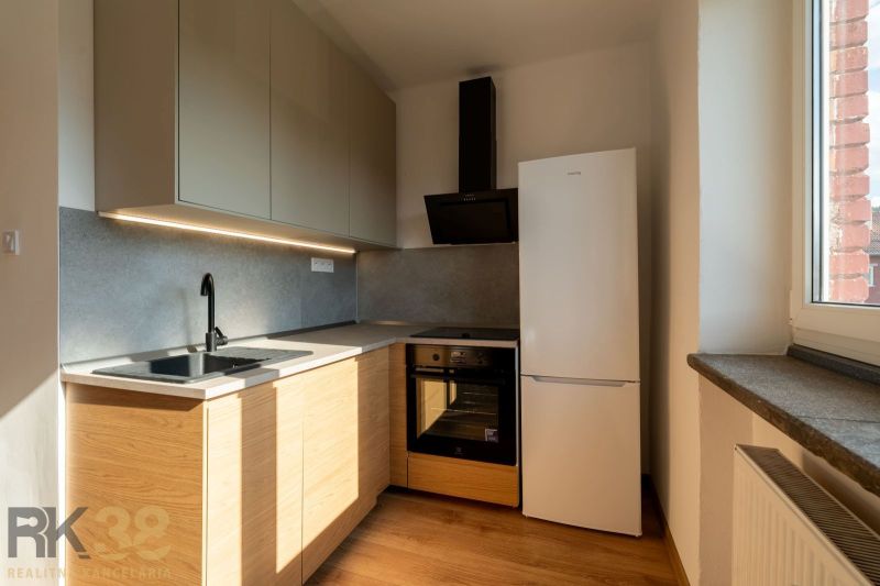 A kitchen in a one-room apartment with a wooden decor floor and appliances.