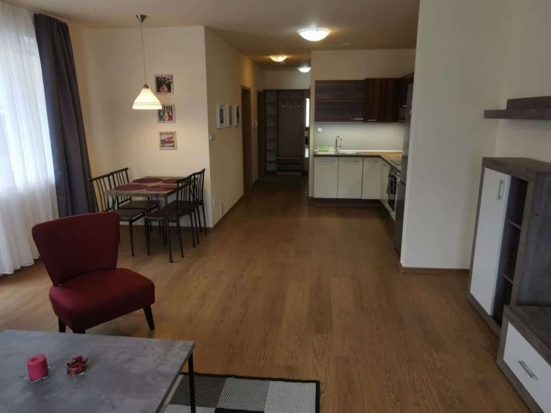 Living room with wood-patterned flooring, dining table, and kitchen unit.