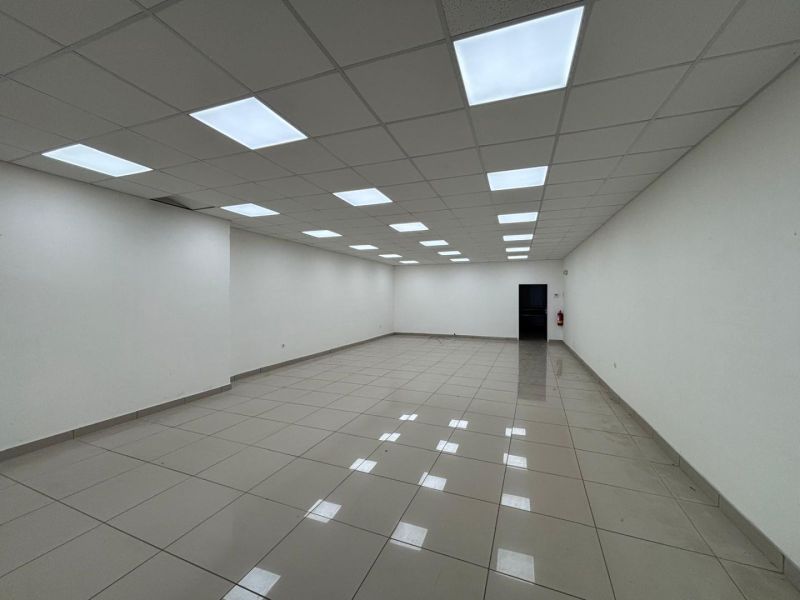 Spacious interior of commercial premises with tiled flooring and a white ceiling full of lighting.