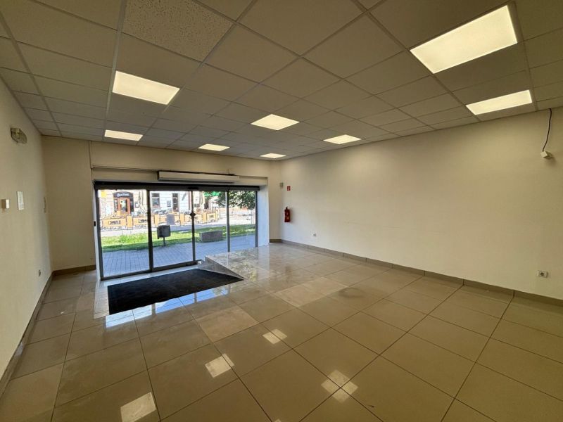 Interior of commercial spaces with tiled flooring, large windows, and a suspended ceiling.