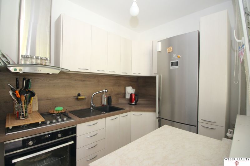 A kitchen in a 2-room apartment with a corner kitchen unit and a silver refrigerator.
