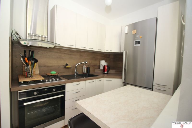 A kitchen in a 2-room apartment with a stainless steel refrigerator and a cooktop with a range hood.