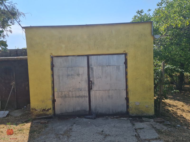 A yellow garage with metal doors near a family house in Komjatice, surrounded by trees.