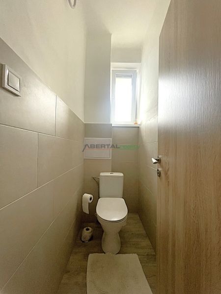 A narrow bathroom with light tiles and a wooden decor floor in a 3-room apartment.
