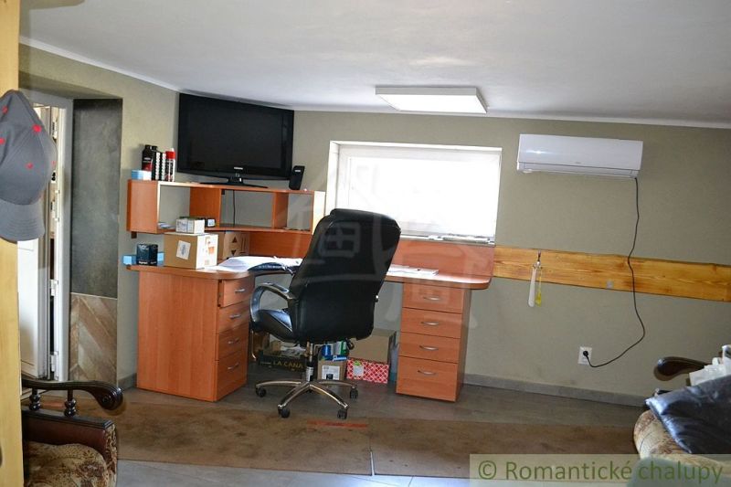 A workspace in a family house with an office desk, shelves, and a television on the wall.