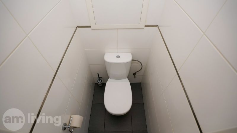 A toilet with white tiles and dark flooring in a 3-room apartment.