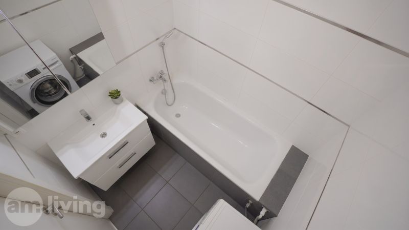 A bathroom with a bathtub, washing machine, sink, and white tiles in a 3-room apartment.