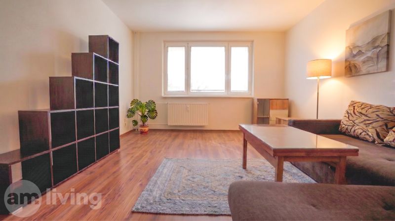 Living room with a sofa, table, floor lamp, and wooden decor flooring in a three-room apartment.