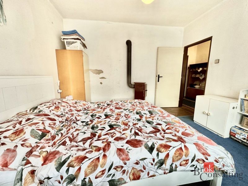 A bedroom in a family house with a bed, stove, and wardrobe, decorated with floral beddings.