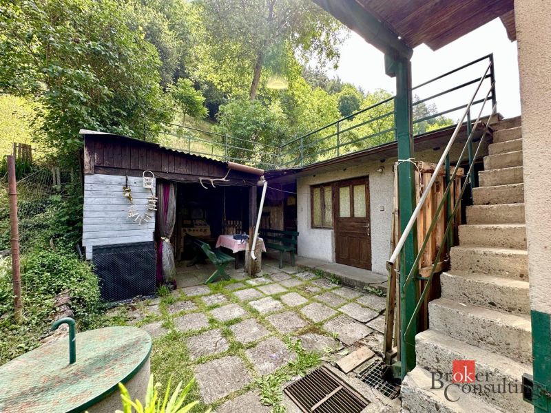The courtyard of a family house in Žiar nad Hronom with a staircase and a wooden annex surrounded by greenery.