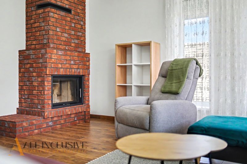 Brick fireplace, comfortable armchair, and shelf in a family house with a wood-patterned floor.