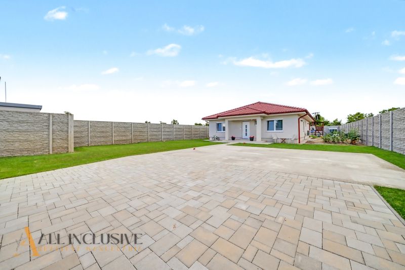 A family house in Vozokany with paving and a grassy garden, bordered by a concrete fence.