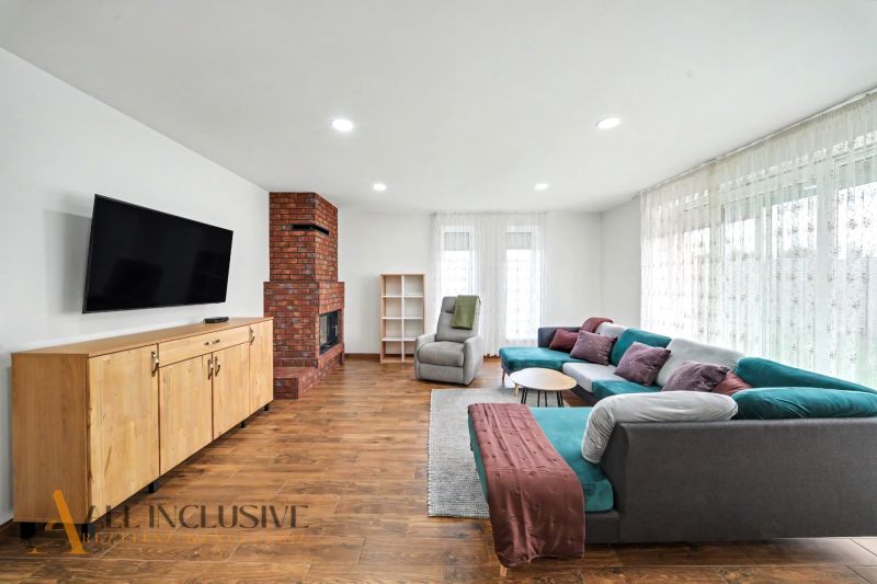 Living room in a family house with a fireplace, a wide sofa, and a wooden-patterned floor.