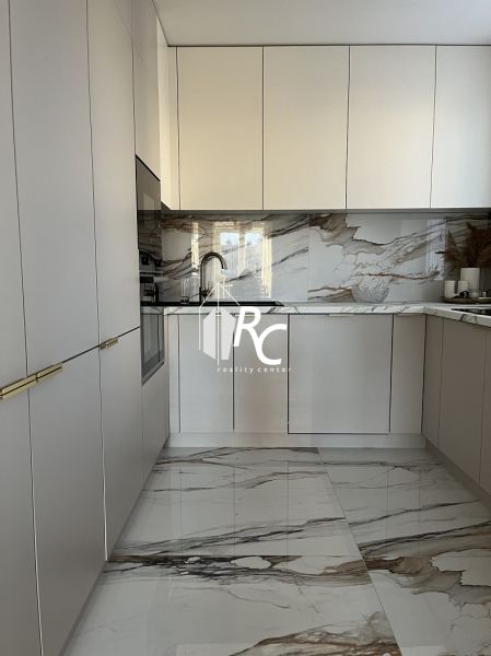 A kitchen in a 2-room apartment with white cabinets and marble tiles.