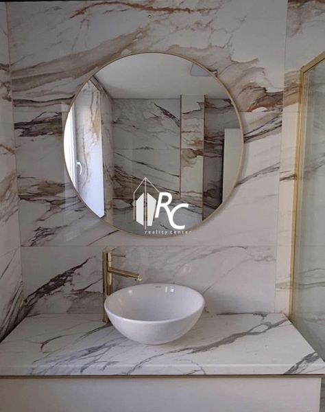 A bathroom with a marble wall and a round mirror in a 2-room apartment.
