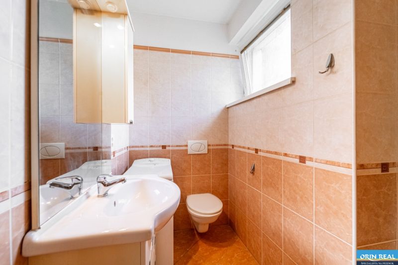 Bathroom in a studio apartment with a sink, cabinet, and toilet, light-colored tiled wall.