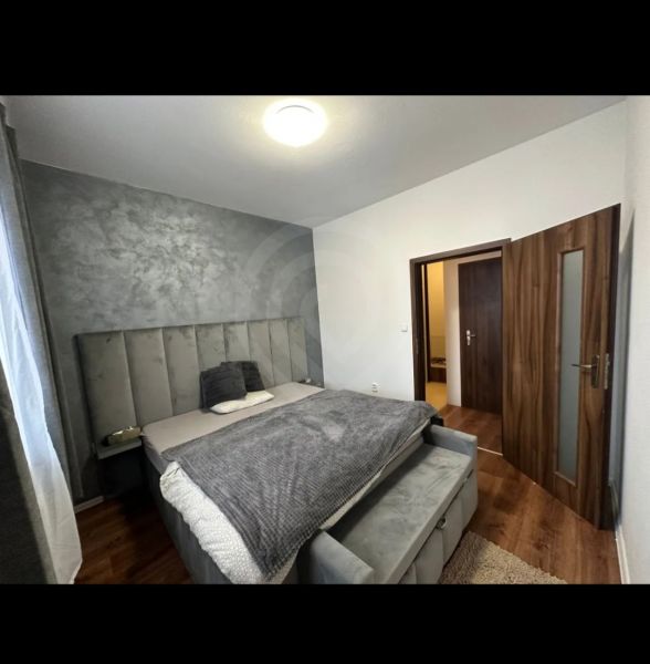 A gray bedroom with a bed and a wooden decor floor in a two-room apartment.