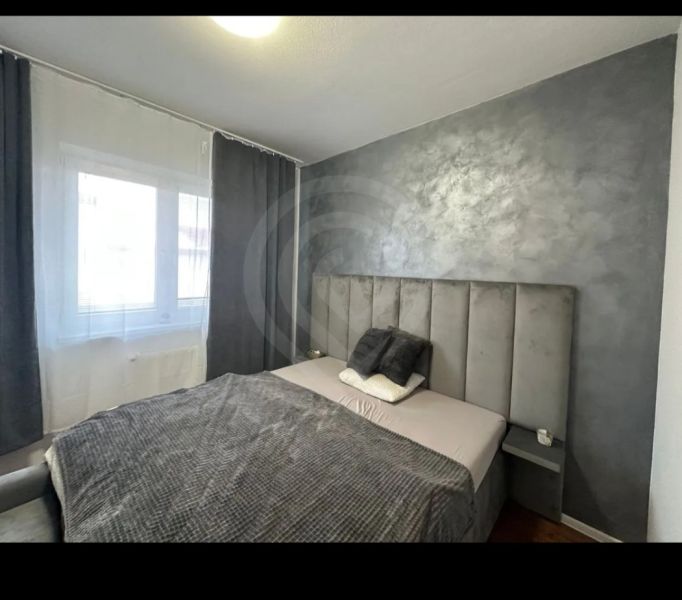 Gray bedroom with a velvet headboard in a 2-room apartment with wood-patterned flooring.