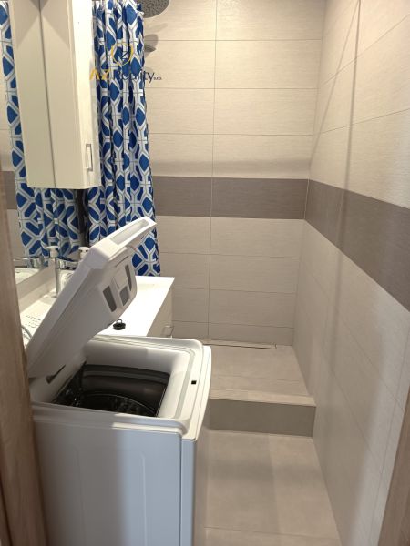 A bathroom with a washing machine and a shower, surrounded by tiles in a studio apartment.