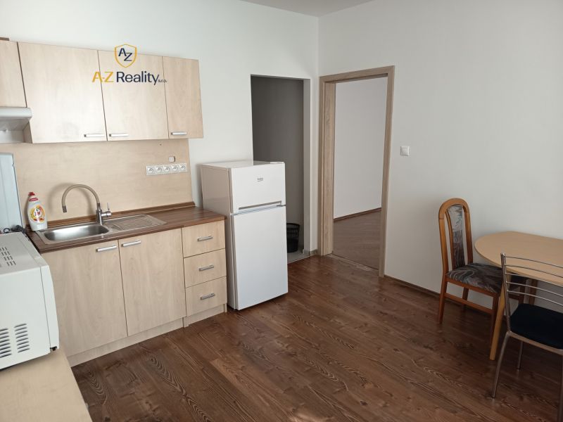 Kitchen unit with refrigerator and table in a studio apartment, floor with wooden decor.