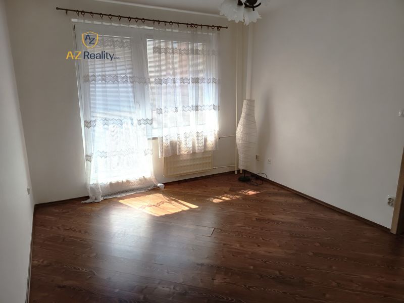 A room in a one-room apartment with a wooden decor floor and curtains.