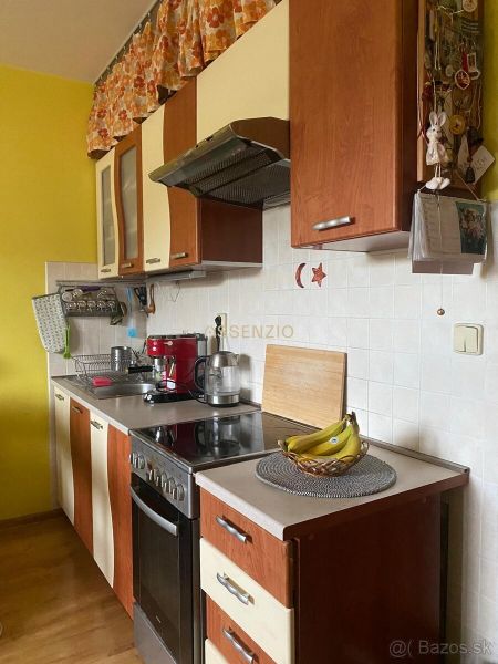 A kitchen in a 2-room apartment with a yellow wall and appliances, flooring with a wooden decor.